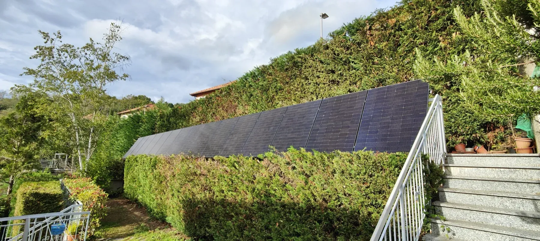 Moduli fotovoltaici montati a pensilina in giardino, davanti alla siepe